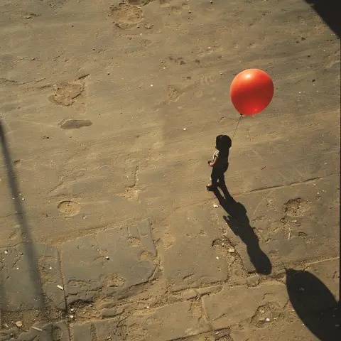 „a photo of a child holding a balloon with its shadow distinctly showing on the ground beside them“