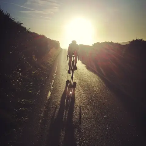 „a photo of a cyclist riding towards the sun, with the shadow stretched long behind“
