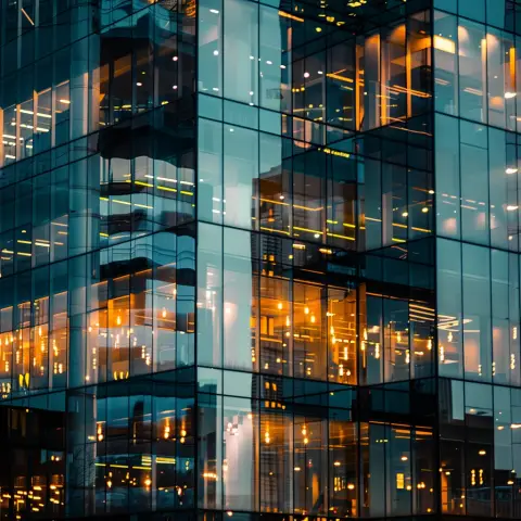 „a photo of city lights reflected on a glass building facade at night“