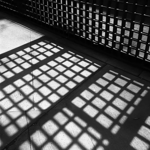 „a photo of geometric shadows cast by a metal grid on a concrete sidewalk“